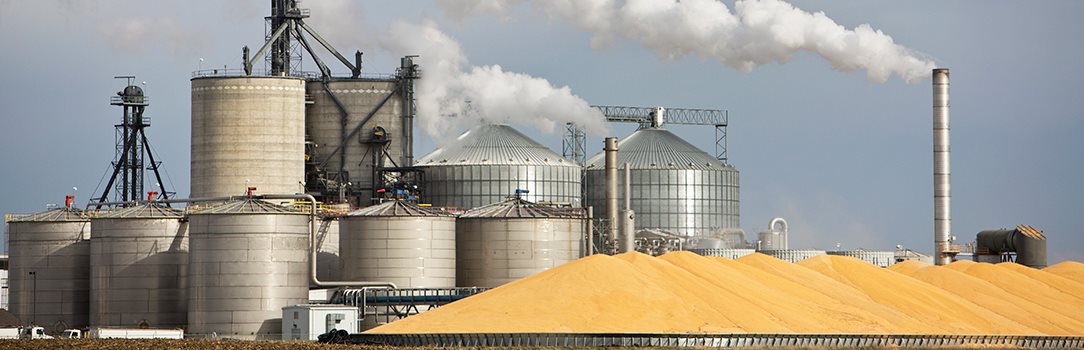 Image of grain silos and refinery with pile of corn in front
