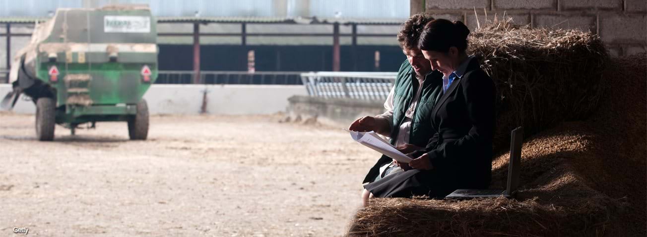 Farmer and wife looking at paperwork with farm scene in the background