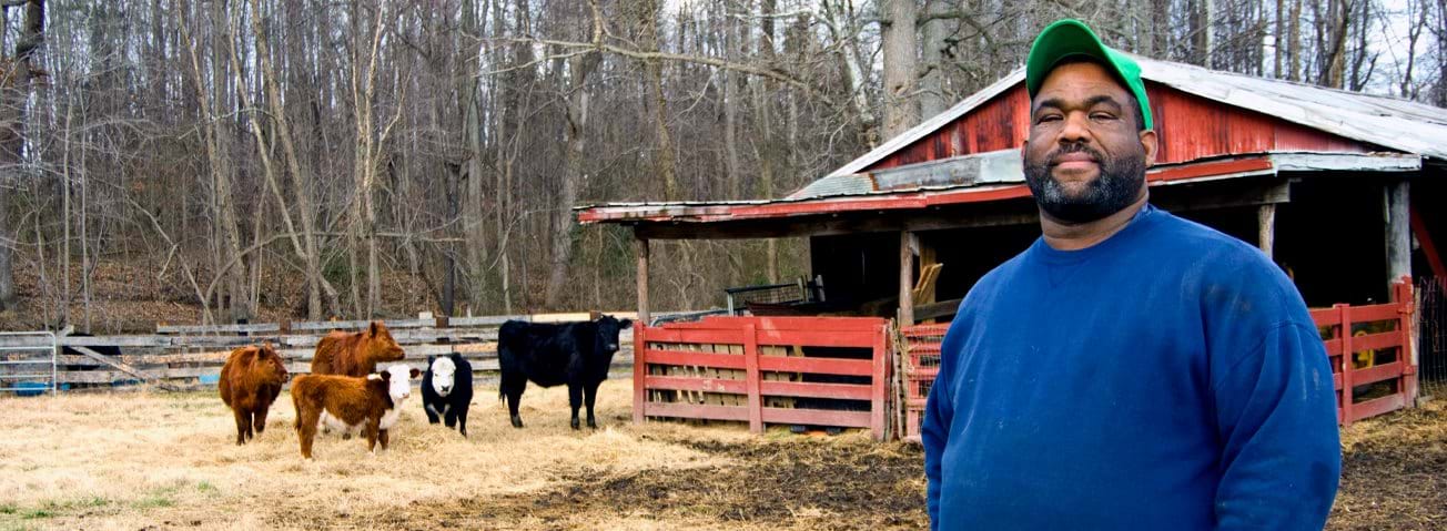 Photo of an African-American man with a barn and cattle in the background.