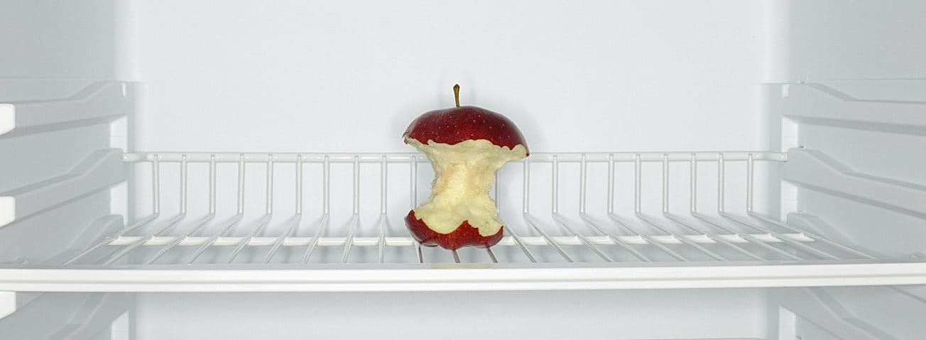 A picture of a mostly eaten apple in an otherwise empty refrigerator. 