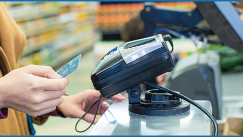 Photo of a woman using a credit/debit card at a grocery store checkout aisle. 
